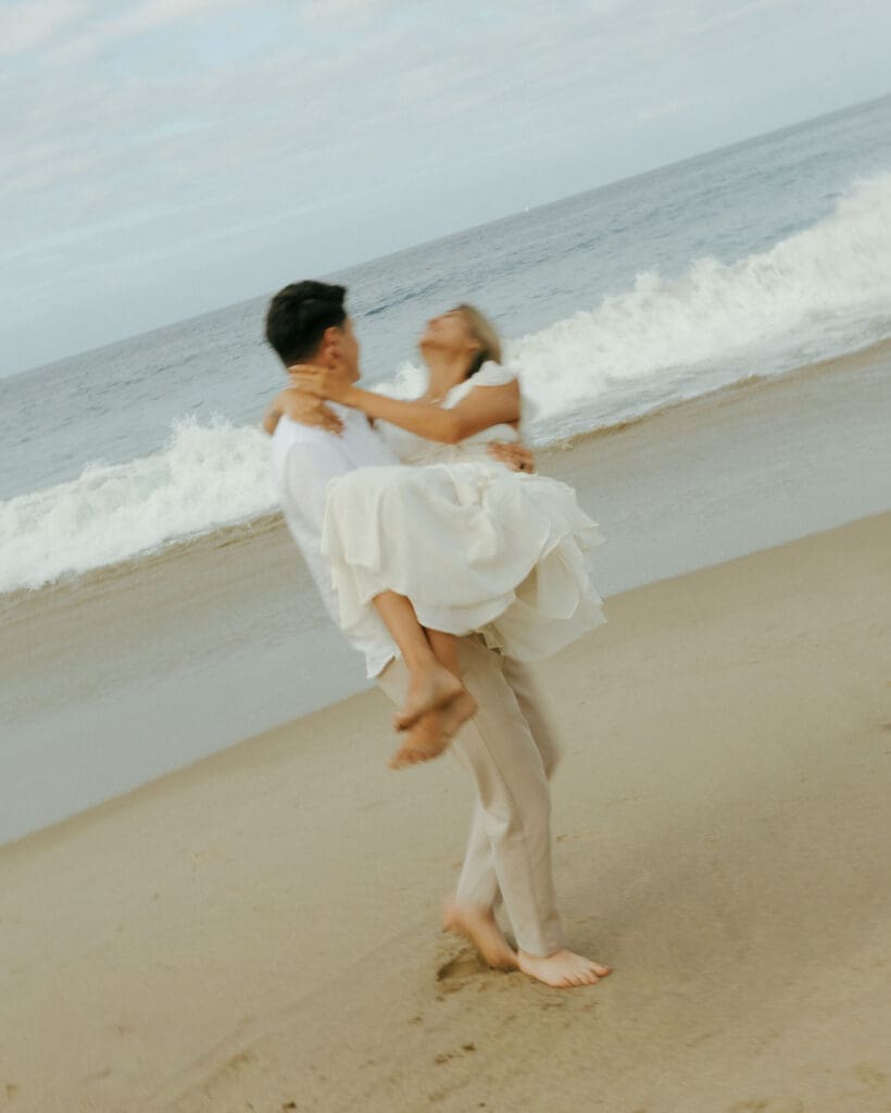 groom picking up his bride at the beach