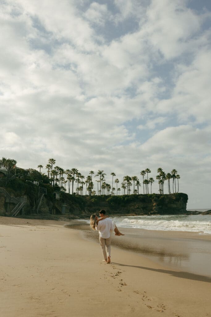 couple walking at laguna beach while the guy is carrying her