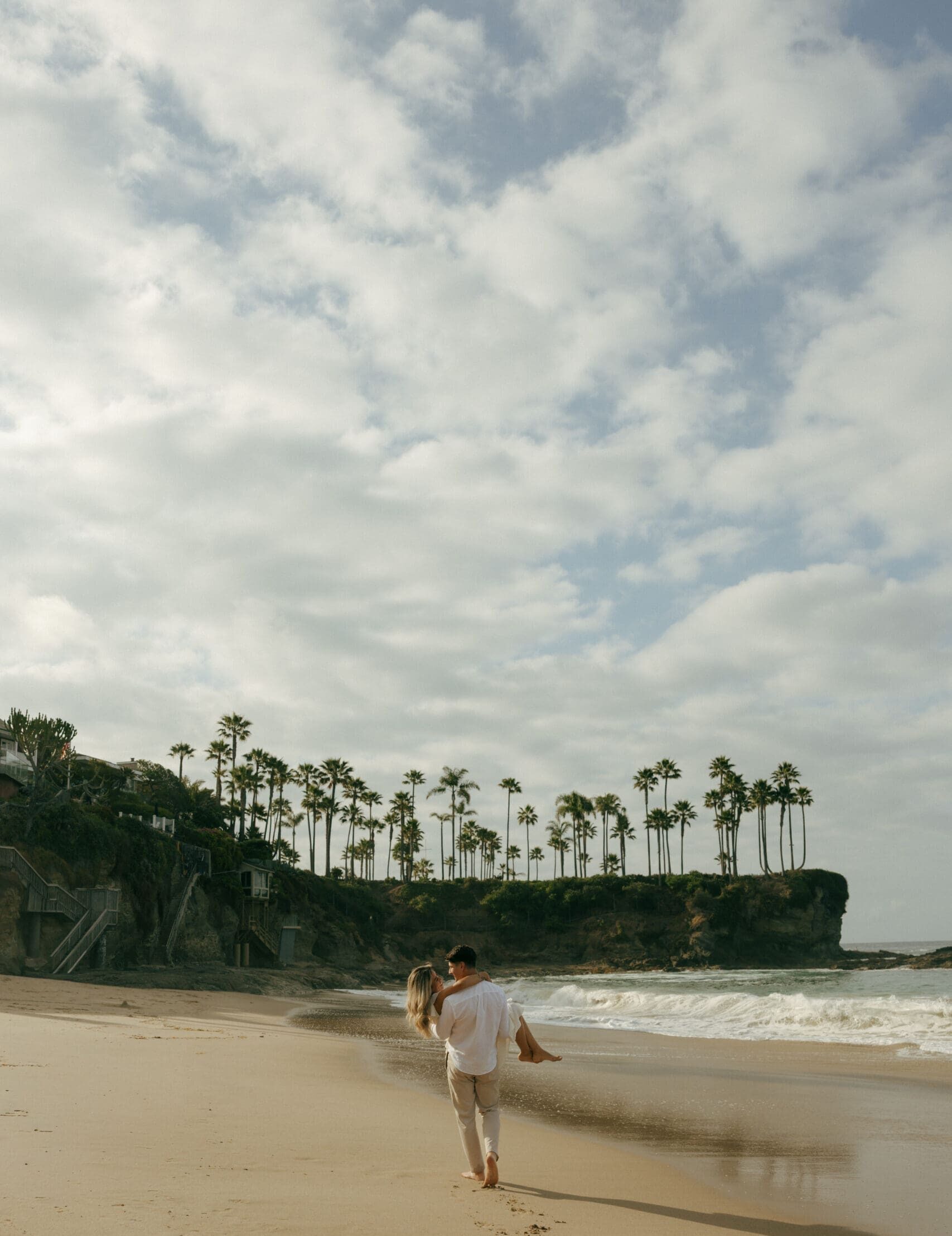 couple walking at laguna beach while the guy is carrying her
