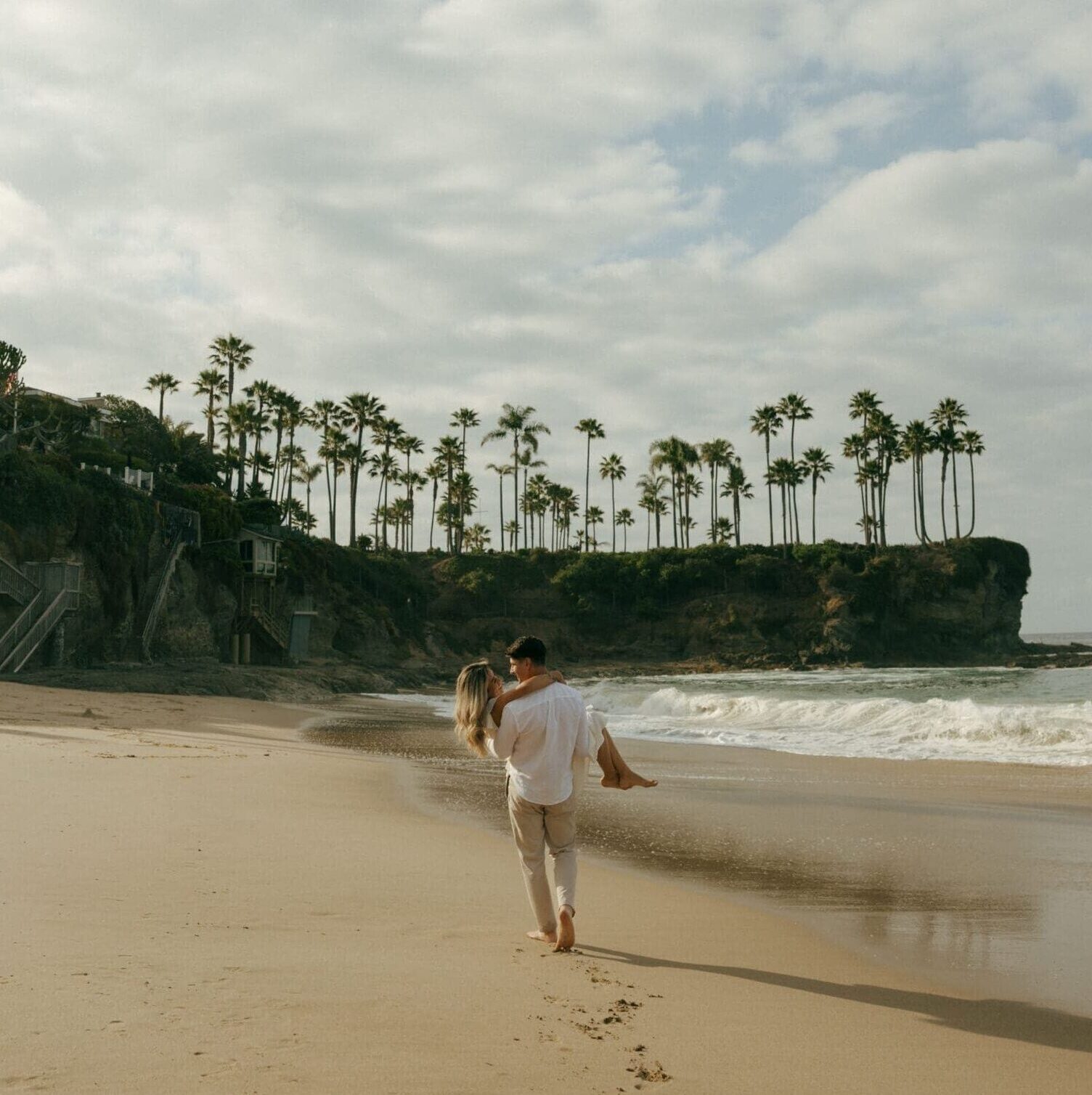 couple walking at laguna beach while the guy is carrying her