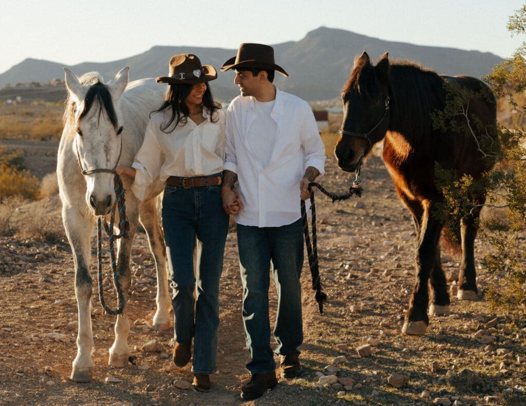 couple laughing and walking with horses