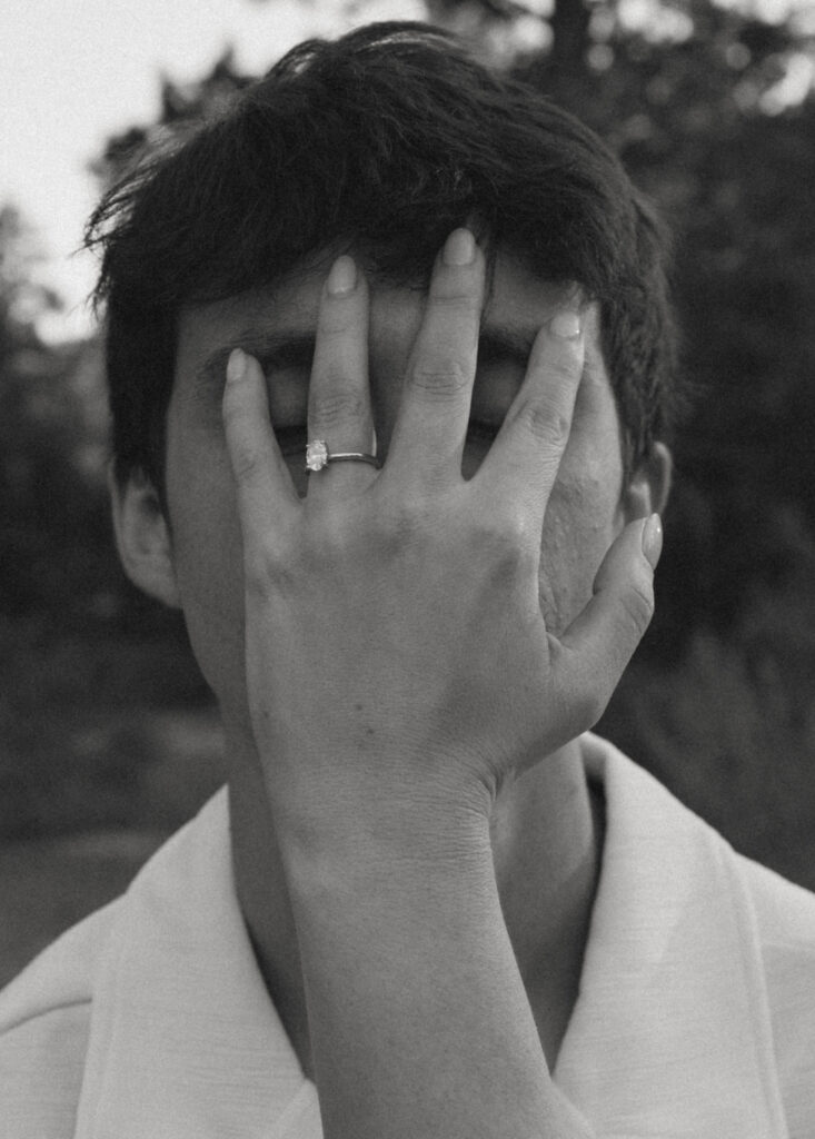 woman showing off engagement ring covering mans face with her hand