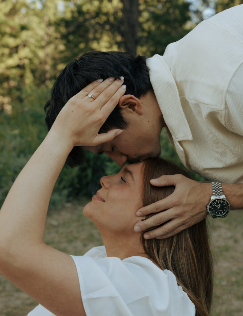 woman sitting as her boyfriend softly kisses her forehead