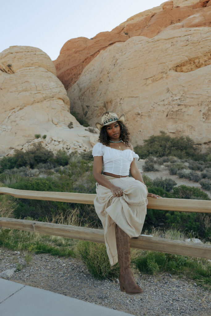 woman sitting on wooden fence in boho clothing at red rock