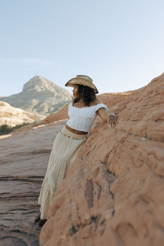 woman leaning on red rocks posing for desert boho portrait session in las vegas
