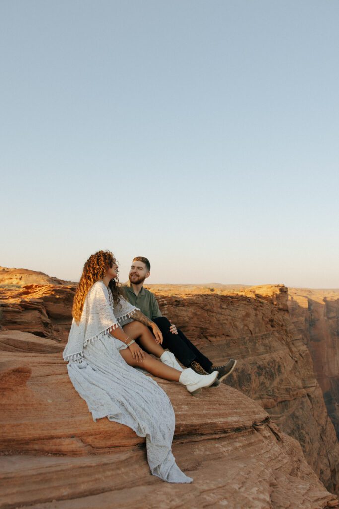 couple sitting on a cliff smiling at each other